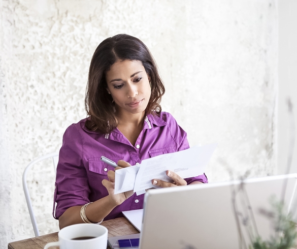 Woman viewing paperwork while sitting at laptop - 12815